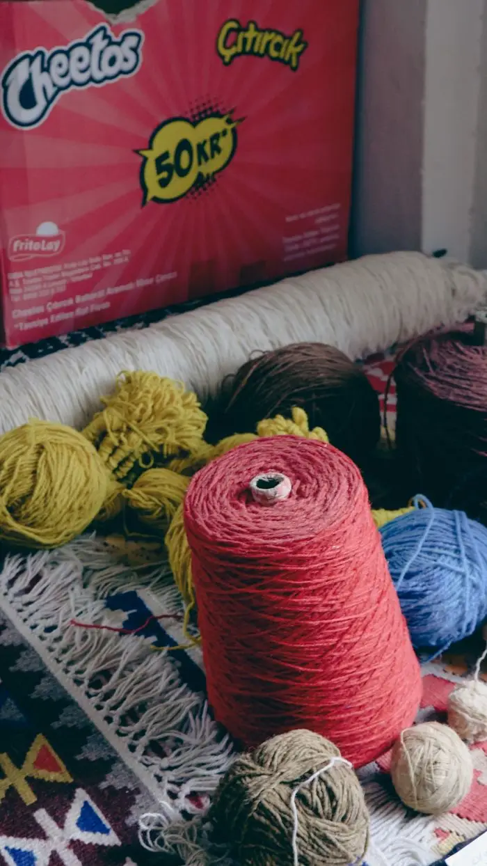 Vibrant yarn balls and spools in various colors arranged on a patterned rug. Ideal for textile and craft themes.