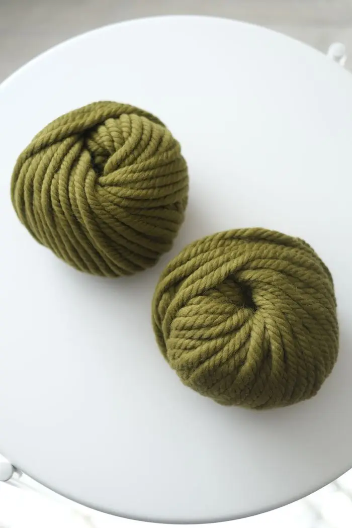 High-angle view of two green wool yarn balls resting on a clean white surface, showcasing texture and color.