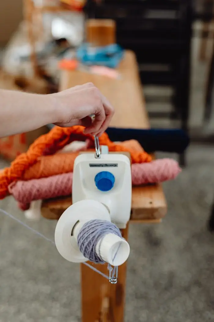 A hand operates a yarn winder with colorful yarn spools in a workshop, creating textile art.